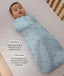 Baby lying in a cot wrapped in a blue ergoPouch Cocoon Swaddle Bag with text highlighting swaddling benefit and TOG rating feature.