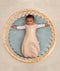 Baby dressed in a Cocoon Swaddle Bag lying in a round bassinet, with two arms out