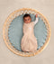 Baby dressed in a Cocoon Swaddle Bag lying in a round bassinet, with one arm out