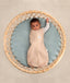 Baby dressed in a Cocoon Swaddle Bag lying in a round bassinet, with one arm out