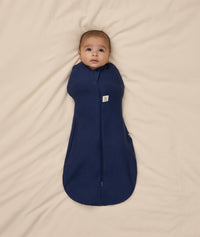 Baby is swaddled in a dark blue ergoPouch Cocoon Swaddle Bag 1.0 TOG with its arms inside.