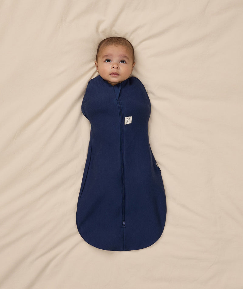 Baby is swaddled in a dark blue ergoPouch Cocoon Swaddle Bag 1.0 TOG with its arms inside.