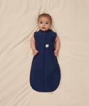 Baby is swaddled in a dark blue ergoPouch Cocoon Swaddle Bag 1.0 TOG with its arms outside.