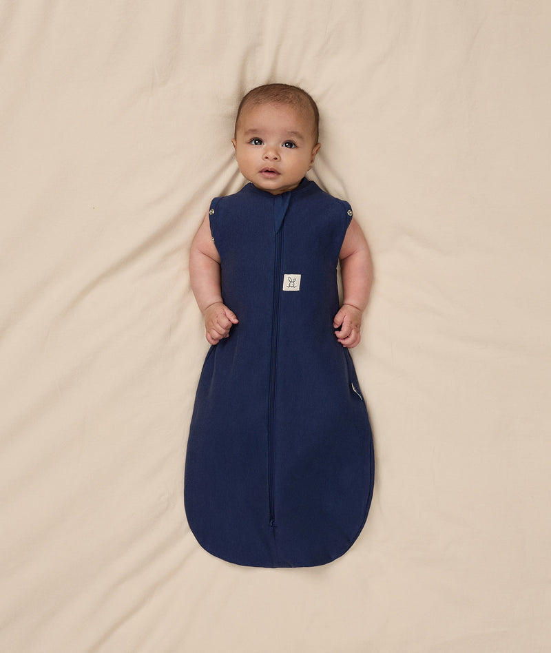 Baby is swaddled in a dark blue ergoPouch Cocoon Swaddle Bag 1.0 TOG with its arms outside.