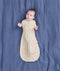 Baby lying on a blue sheet background, wearing a patterned Cocoon Swaddle Bag with both arms out.