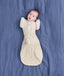 Baby lying on a blue blanket wearing a cream patterned Cocoon Swaddle Bag and a Butterfly Cardi.