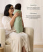 A mum sitting in an armchair holding a swaddled baby in a sage green floral Cocoon Swaddle Bag, with text callouts highlighting swaddling benefits and TOG ratings.