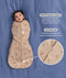 Baby lying on a blue blanket wearing a Cocoon waddle Bag with text highlighting organic cotton and two-way zip.