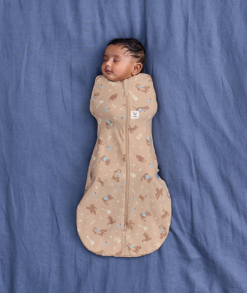 Sleeping baby lying on a blue sheet background, wearing an ergoPouch Cocoon Swaddle Bag 1.0 TOG made from soft, organic cotton.