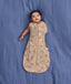 Baby lying on a blue fabric background wearing a tan patterned Cocoon Swaddle Bag with one hand out.