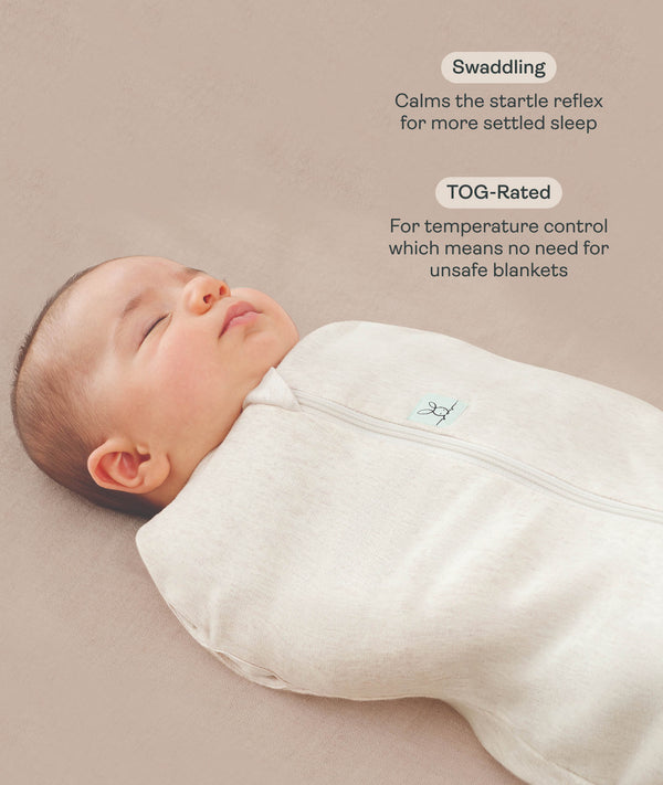 Close-up view of a sleeping baby being swaddled in an ergoPouch Cocoon Swaddle Back Oatmeal Marle with text highlighting swaddling benefit and TOG rating feature.