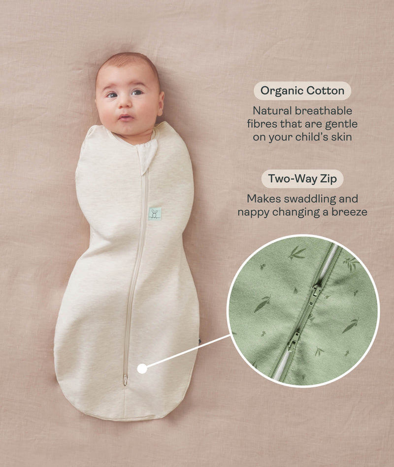 Baby lying on a beige surface wrapped in a Cocoon Swaddle Bag with text highlighting organic cotton fabric and two-way zip feature and a close-up inset of the dual zippers. 