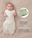 Baby lying on a beige fabric in an oatmeal-coloured swaddle bag with arms out, featuring callout text highlighting press studs and a bell-shaped design.