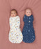 Two babies lying on a pink surface wearing ergoPouch Cocoon Swaddle Bags. One wearing a 2.5 TOG Swaddle Bag in Daydream, while the other wearing a 1.0 TOG Swaddle Bag in Starbeam