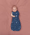 Baby lying on a pink surface wrapped in a blue Cocoon Swaddle Bag 1.0 TOG, one arm out