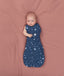Baby lying on a pink surface wrapped in a blue Cocoon Swaddle Bag 1.0 TOG, one arm out