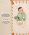 Baby lying in a wooden cot wearing a sage green patterned swaddle bag over footed layer, with product feature text callouts highlighting organic cotton fabric and two-way zip features.