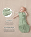 Baby lying on a beige surface in a green patterned swaddle bag with arms out, featuring callout text highlighting press studs and a bell-shaped design.
