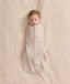 An overhead view of a baby swaddled in a patterned beige Cocoon Swaddle Bag, lying flat on a cream-colored blanket.
