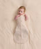 Baby lying on a cream blanket, wearing a patterned Cocoon Swaddle Bag with both arms out