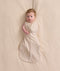 An overhead view of a baby lying flat on a cream-colored sheet, wearing a patterned Cocoon Swaddle Bag with one arm extended out.
