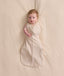 An overhead view of a baby lying flat on a cream-colored sheet, wearing a patterned Cocoon Swaddle Bag with one arm extended out.