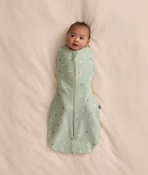 Baby swaddled in a green floral Cocoon Swaddle Bag 1.0 TOG, lying on a cream-coloured blanket.
