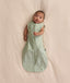 Baby lying on a cream blanket, wearing an ergoPouch Cocoon Swaddle Bag 1.0 TOG with both arms out.