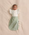 Baby lying on a cream -coloured blanket, wearing a sage green floral-patterned Cocoon Swaddle Bag layered with a Butterfly Cardi over top