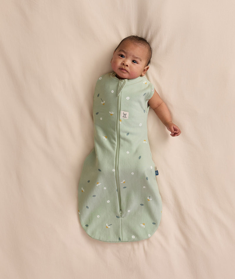Baby wearing a sage green floral-patterned Cocoon Swaddle Bag with one arm extended out