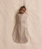 Baby lying on a cream blanket, swaddled in an ergoPouch Cocoon Swaddle Bag 1.0 TOG Taupe Marle