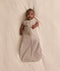 Baby lying on a cream blanket, wearing an ergoPouch Cocoon Swaddle Bag with both arms out