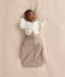 Baby lying on a cream-coloured blanket wearing a Cocoon Swaddle Bag layered with a Butterfly Cardi over top.