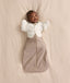 Baby lying on a cream-coloured blanket wearing a Cocoon Swaddle Bag layered with a Butterfly Cardi over top.