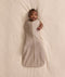 Baby lying on a cream-coloured blanket, wearing an ergoPouch Cocoon Swaddle Bag with one arm extended out.
