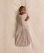 Baby lying on a cream-coloured blanket, wearing an ergoPouch Cocoon Swaddle Bag with one arm extended out.