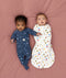 Two babies lying on a pink surface, one wearing a blue slim-fit Long Sleeve Layer, while the other wearing a white Cocoon Swaddle Bag with colourful print.