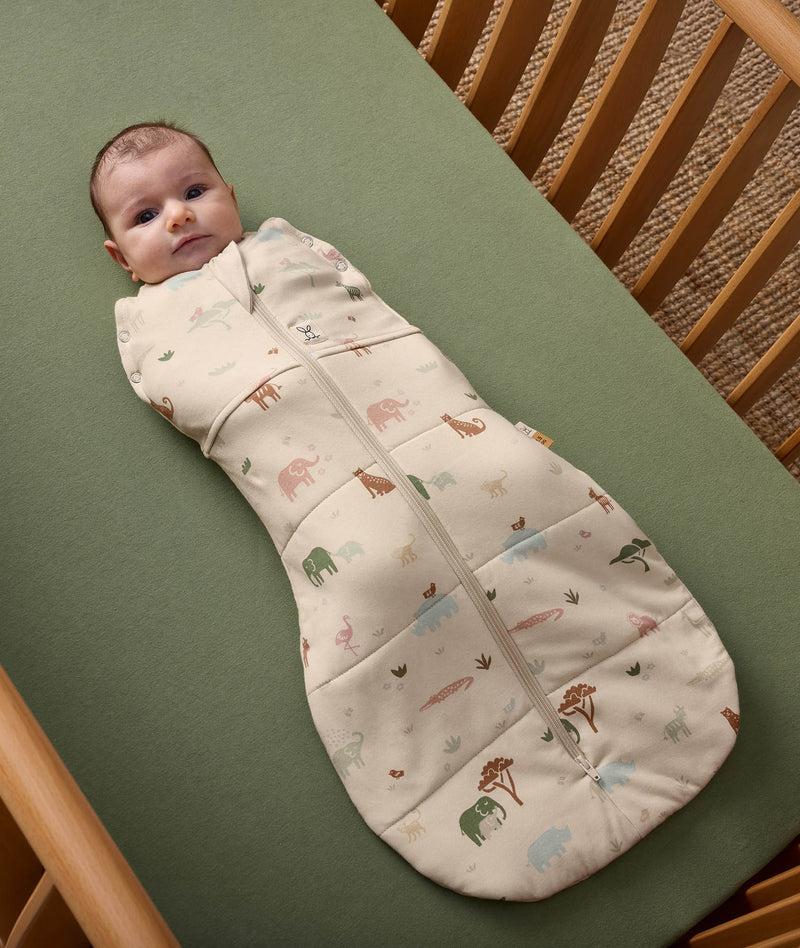 Baby is lying in a cot wearing an ergoPouch Cocoon Swaddle Bag with its arms secured inside.