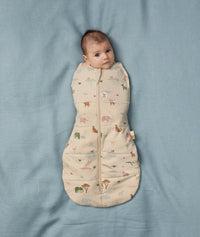Baby lying on a soft blue sheet wearing an ergoPouch Cocoon Swaddle Bag with its arms securely swaddled inside.
