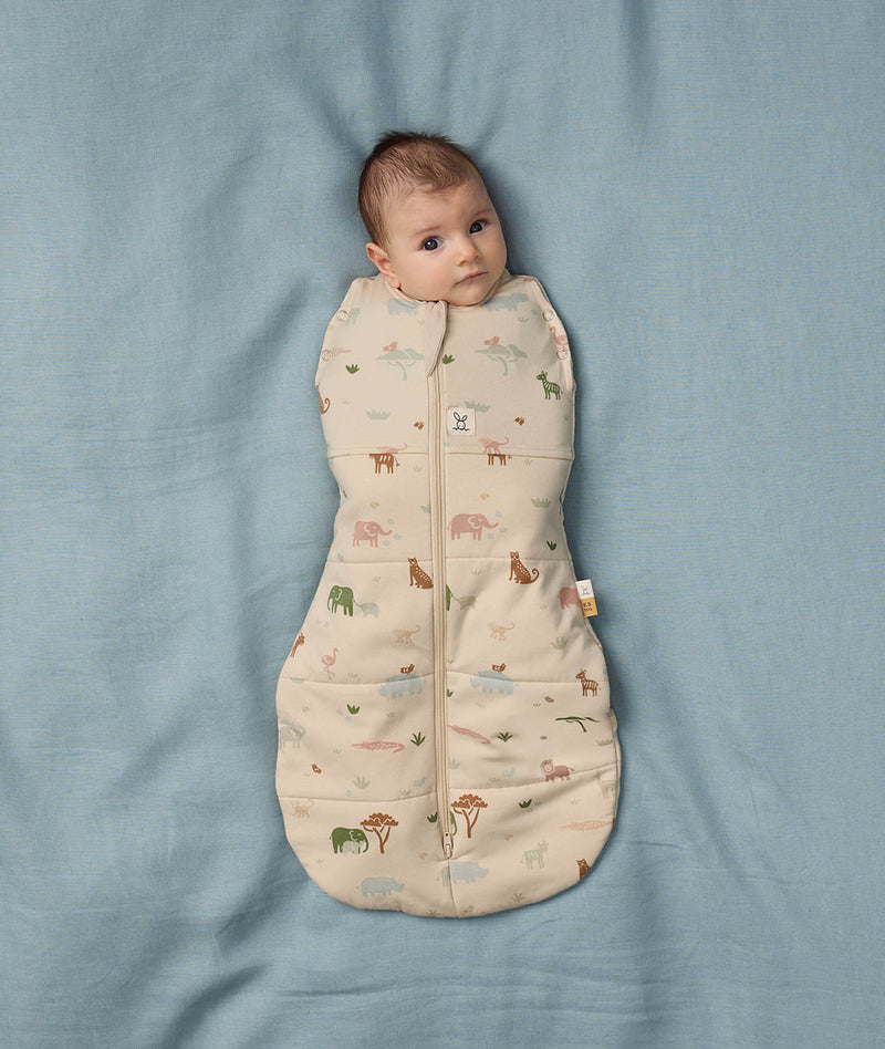 Baby lying on a soft blue sheet wearing an ergoPouch Cocoon Swaddle Bag with its arms securely swaddled inside.