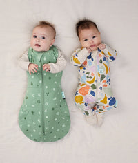 Two babies lying side by side. One wearing a 2.5tog Cocoon Swaddle Bag, while the other is wearing a Long Sleeve Layer