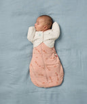 A sleeping baby is securely swaddled in a Cocoon Swaddle Bag with a Butterfly Cardi for an arms-out position.
