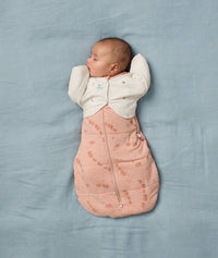 A sleeping baby is securely swaddled in a Cocoon Swaddle Bag with a Butterfly Cardi for an arms-out position.