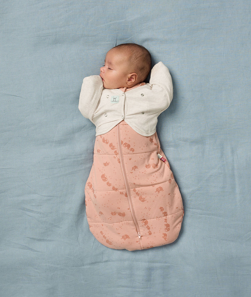 A sleeping baby is securely swaddled in a Cocoon Swaddle Bag with a Butterfly Cardi for an arms-out position.