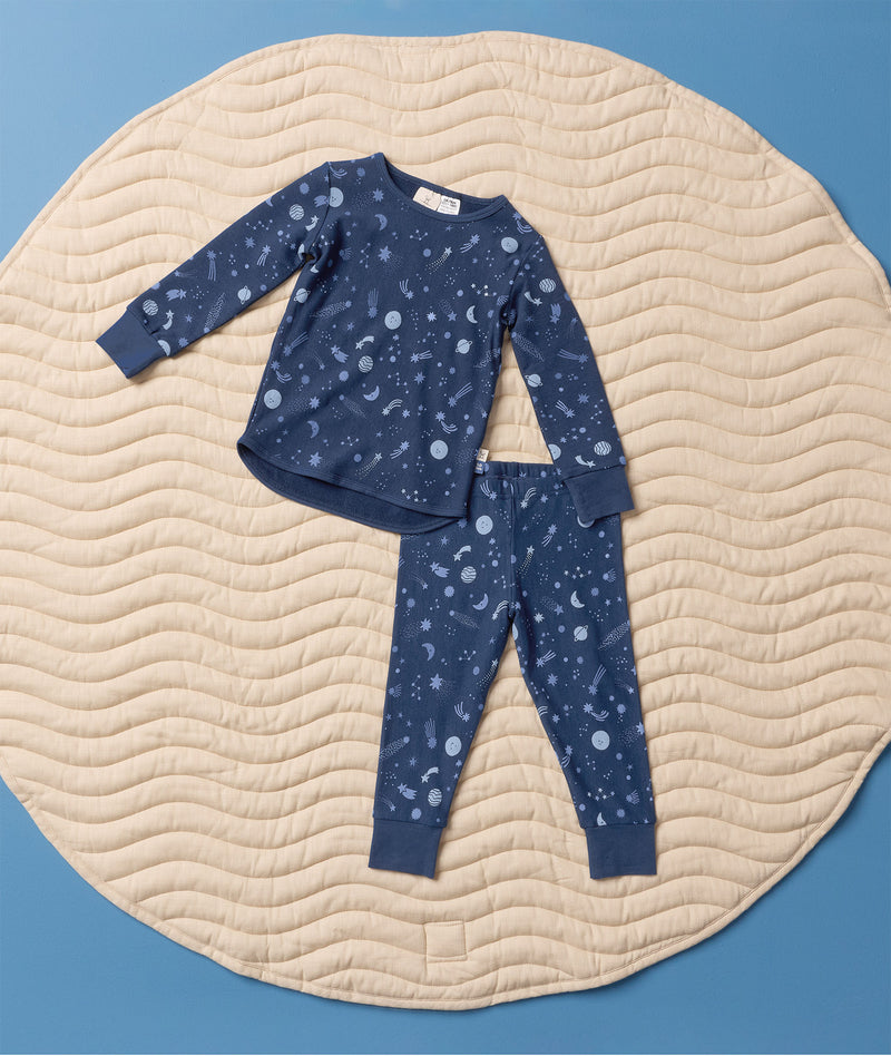 Blue Long Sleeve Pyjama set with a moon-and-star print, laid flat on a round quilted mat against a light blue background.