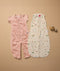 Two baby sleep suits laid flat on a beige surface. The left suit is pink with short sleeves and an elephant print, featuring a zipper down the front and separated legs. The right suit is sleeveless, cream-colored with a multicolored animal print, also with a front zipper.