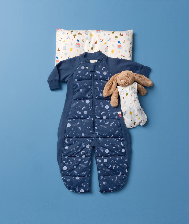 Flatlay of the ergoPouch  Sleep Suit Bag 3.5 TOG, Toddler Pillow in Daydream, with a teddy bear dressed in a Doll Sleeping Bag