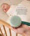 An adult hand holds a round, mint-green Drift Away white noise machine next to a cot where a baby is peacefully sleeping. A text box highlights 