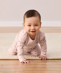 An infant is crawling towards the camera, wearing pink ergoPouch long-sleeve baby pyjamas with an all-over daisy print.