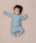 Baby lying on a soft pink sheet, wearing ergoPouch Long Sleeve Baby Pyjamas with press studs opening on the shoulder for easy wear.